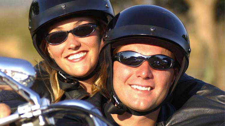 A helmeted woman smiles as she holds tight to her helmeted driver.